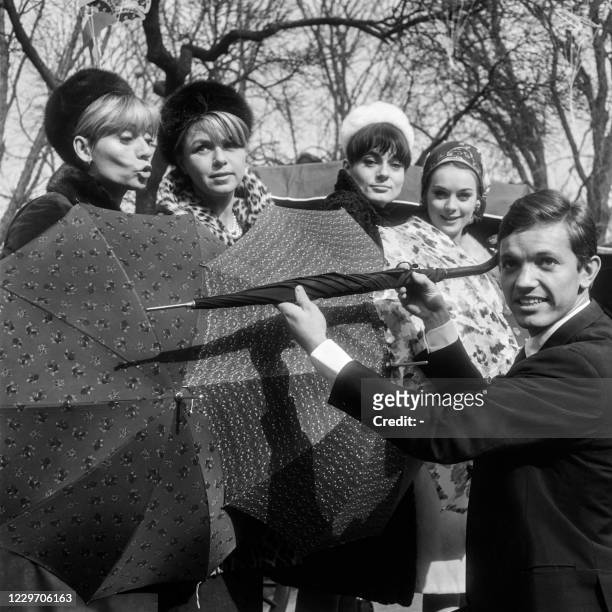 Picture taken on February 23, 1965 at Paris showing French singer Frank Alamo giving umbrellas to the singer Annie Cordy and to the actresses...