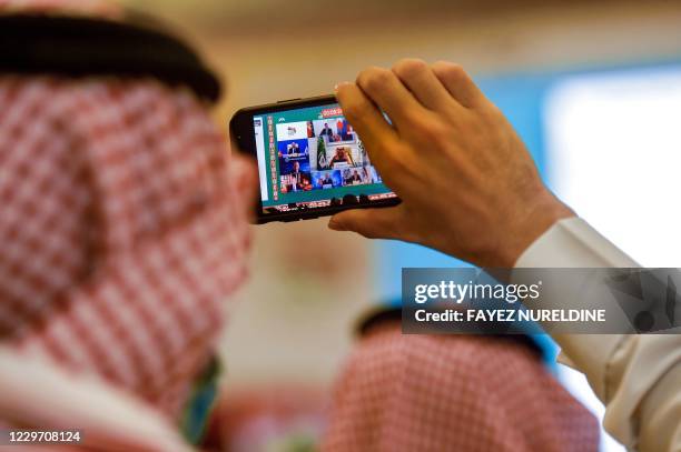 Man uses a phone to film a projected screen at the International Media Centre in Saudi Arabia's capital Riyadh on November 21, 2020 showing Saudi...