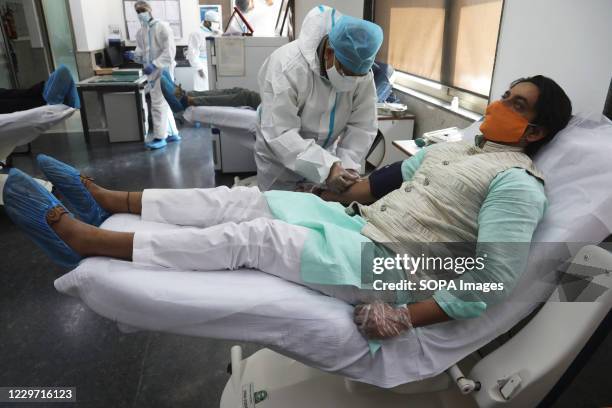 Lab technician dressed in a protective suit collects blood from a donor during the blood donation camp for corona warriors at Indian Red Cross...