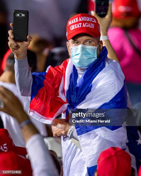 Un simpatizante de Trump envuelto en una bandera cubana mira hacia la multitud durante el rally Make America Great Again Victory, en el Signature...