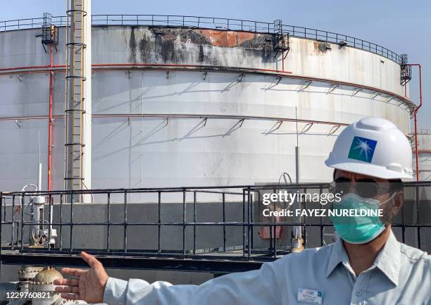 An employee at the Saudi Aramco oil facility, mask-clad due to the COVID-19 coronavirus pandemic, gestures while standing near a damaged silo, at the...