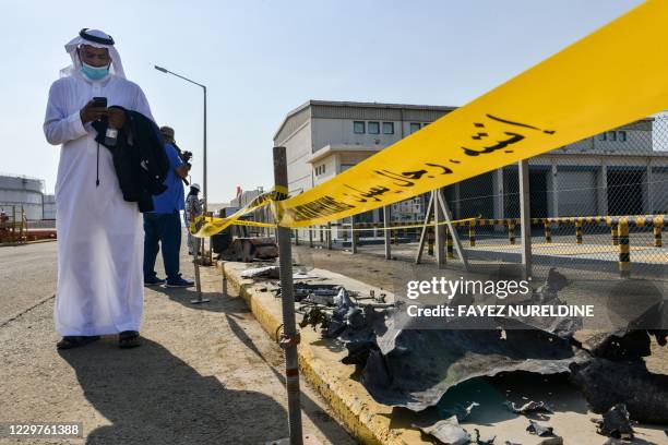 Man, mask-clad due to the COVID-19 coronavirus pandemic, browses his phone while standing near debris following an attack at the Saudi Aramco oil...