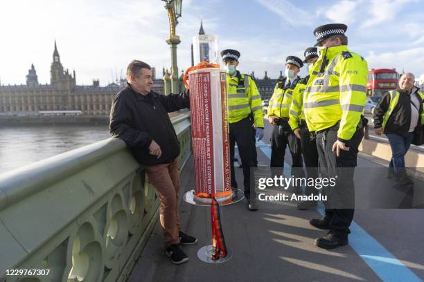 Protester with a model Covid 19 vaccine syringe is detained by police officers at a demonstration against a Covid 19 vaccine education event taking...