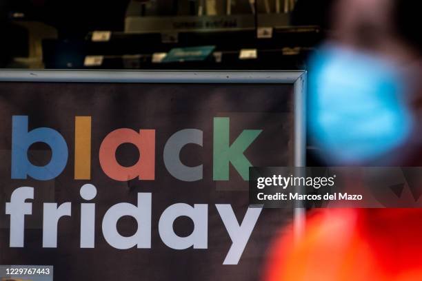 Woman wearing a face mask to protect against the Coronavirus passing by a sign that announces Black Friday on the display window of a shop in...