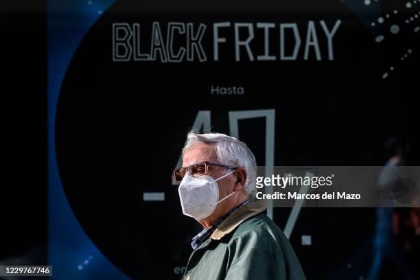 Man wearing a face mask to protect against the Coronavirus passing by a sign that announces a price discount for Black Friday on the display window...
