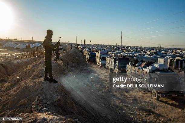 Masked guard keeps watch as trucks transports Syrians leaving the Kurdish-run al-Hol camp holding relatives of alleged Islamic State group fighters,...