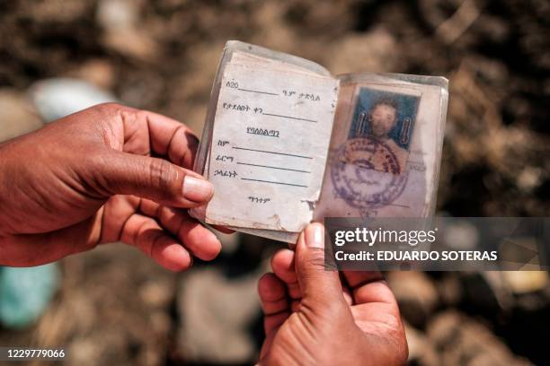 This photograph taken on November 21, 2020 shows a man holding a ID that he found, over a collective grave of victims that were allegedly killed in...