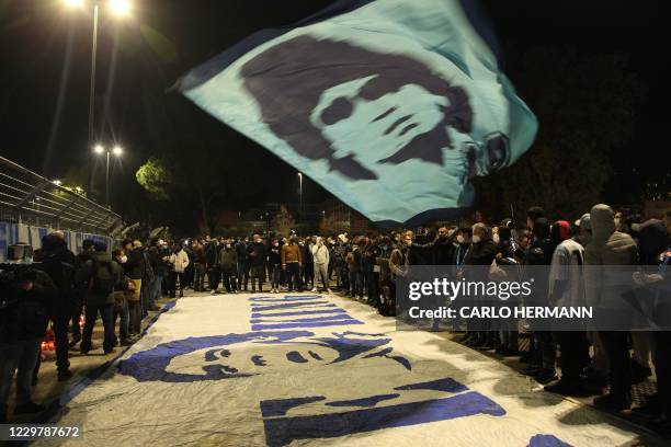 People gather at the main entrance of the San Paolo stadium in Naples on November 25, 2020 waving a flag at the effigy of Argentinian football legend...