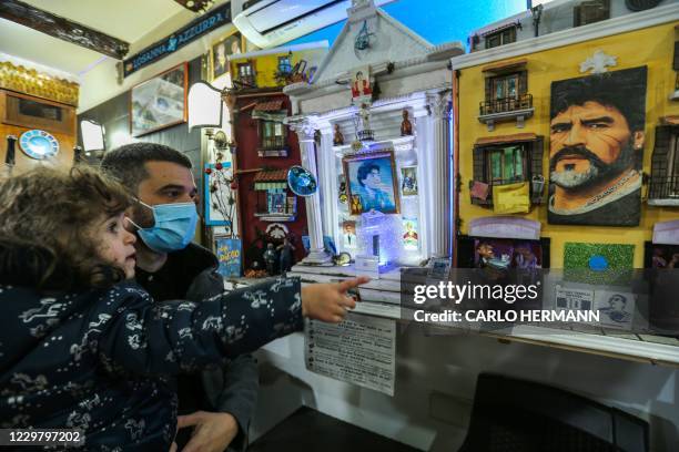 Man holding a child view a box purportedly containing a lock of Diego Maradona's hair, and a small altar dedicated to Argentinian football legend...