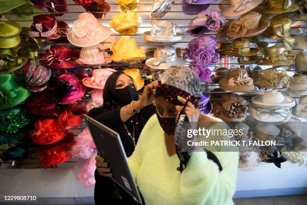 Meeka Robinson Davis, owner of One-Of-A-Kind Hats, helps customer Elena Jean Tucker try on a crosshatch headband with matching face mask inside her...