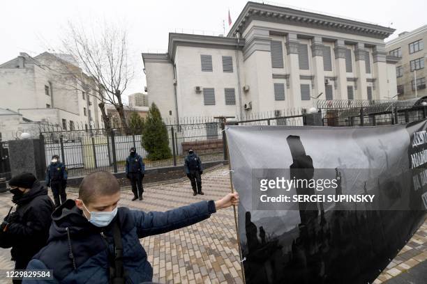 Ukrainian far-right activist holds a placard outside the Russian embassy in Kiev on November 28, 2020 during their protest action called "You killed...