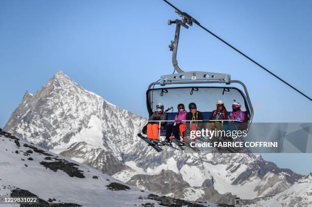 Skiers, some wearing protective face masks against the spread of the Covid-10 , ride a ski lift before hitting the slopes above the ski resort of...