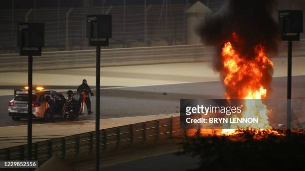 Stewards watch as Haas F1's French driver Romain Grosjean's car burns during the Bahrain Formula One Grand Prix at the Bahrain International Circuit...