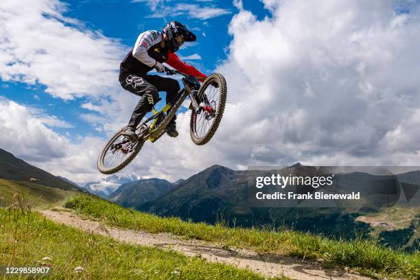 Downhill cyclist is jumping in the Mottolino Bike Park, surrounding mountains of Livigno in the distance.