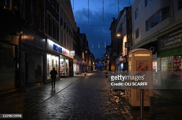 Pedestrian walks past a white telephone box along an almost deserted street in Hull, in north-east England on November 30, 2020. - Hull will return...