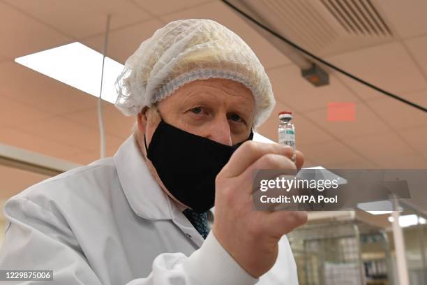 Prime Minister Boris Johnson, wearing a hair net and face covering, poses for a photograph with a vial as he views the last minute quality testing of...