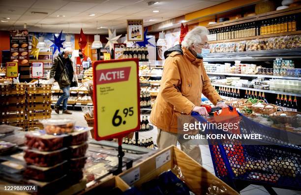 Customer wears a face mask as he pushes a trolley in a supermarket in Amsterdam on December 1, 2020. - In public interior spaces it is required now...