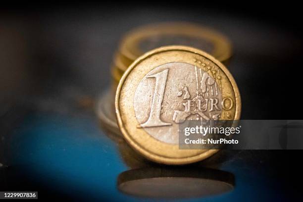 Close up of isolated one Euro coin the main currency of the European Union, money stacked on euro coins in the background on a reflecting surface....