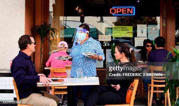 Waitress serves guests as people dine outdoors in Pasadena, California, the only city in Los Angeles County still allowing that service on December...