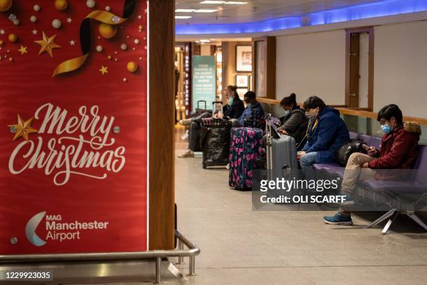Members of the public wait next to a poster wishing passengers a merry Christmas, at Terminal 1 of Manchester Airport in Manchester, northern England...