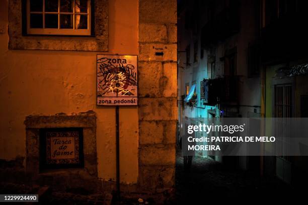 Pedestrian is silhouetted in an empty street of the Alfama neighbourhood in Lisbon on November 27, 2020. - Fado houses had already lost most of their...