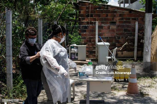 Health worker receives help from an employee to put on PPE before before performing COVID-19 testings at the Emergency Care Unit Colubandê on...