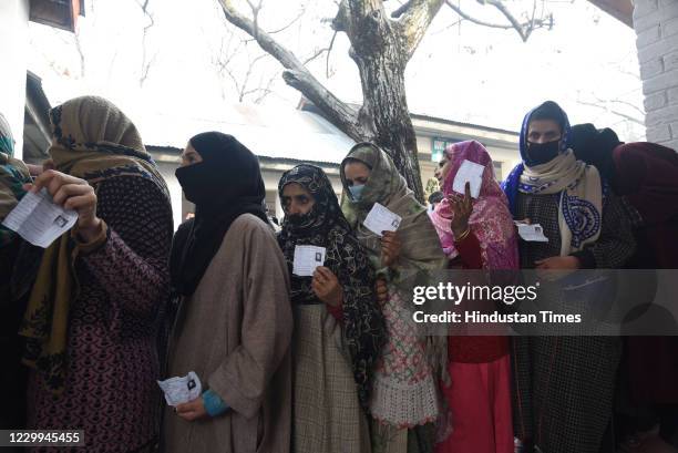 Voters wearing facemasks show their voter id as they queue up to cast their vote during the third phase of District Development Council Election in...