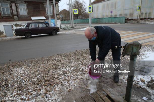 Man wearing a protective face mask pours water on the street, on December 5, 2020 in Staritsa, located on the Volga river, 250 kilometers northwest...