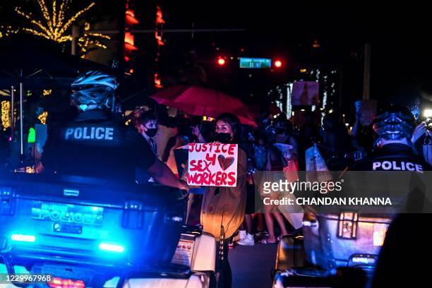 Activists and sex workers hold up signs near police as they participate in a "Slut Walk" in Miami beach, Florida on December 5, 2020. - Activists and...