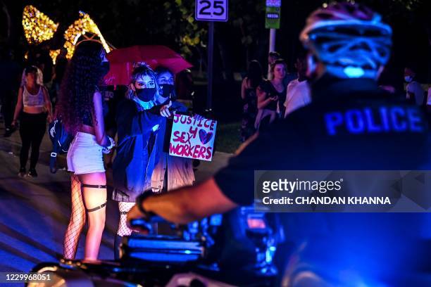 Activists and sex workers hold up signs near police as they participate in a "Slut Walk" in Miami beach, Florida on December 5, 2020. - Activists and...
