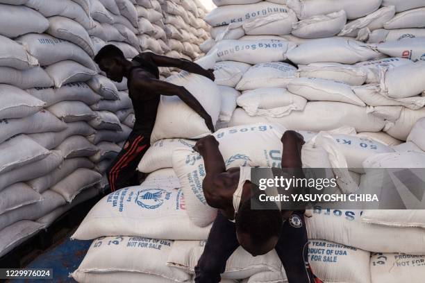 Sudanese local community members carry to deliver sacks of sorghum for Ethiopian refugees who fled the Ethiopia's Tigray conflict in a warehouse...