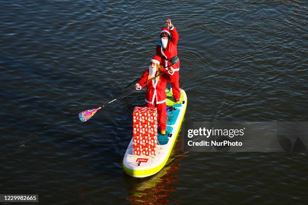 Stand up paddleboarding surfers wearing Santa Claus costumes float on Vistula River during a charity event on Saint Nicholas Day in Krakow, Poland....