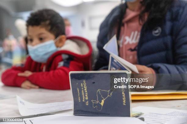 Boy wearing a face mask sits with a woman, as she gets her new El Salvadoran passport. The El Salvadoran Consulate is responsible for processing...