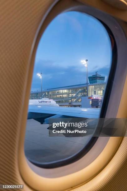 Lufthansa Airbus A350 aircraft and the Terminal of the airport as seen early morning in the dawn, sunrise time from another airplane window, parked...