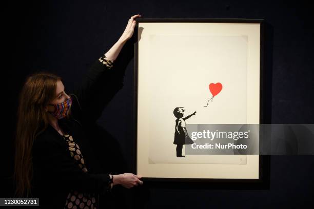 Member of staff wearing a face mask poses with 'Girl with Balloon', by British artist Banksy, estimated at 120,000-180,000GBP, during a photo call...