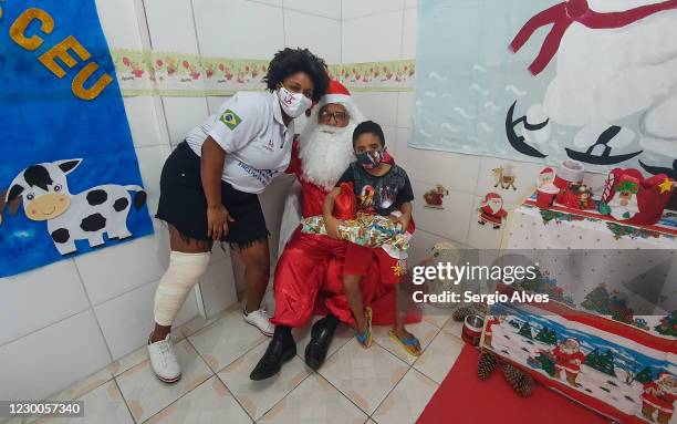 Jaqueline Laureano and Thiago Venancio pose with a person dressed as Santa Claus at the Christmas party at Uniao de Mulheres Pro Melhoramentos da...