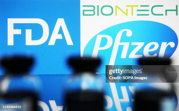 In this photo illustration, vials are seen in front of the Food and Drug Administration of the United States and Pfizer Pharmaceutical company logos....