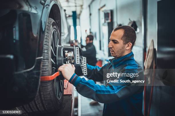 twee jonge auto mehanic plaatst de apparatuur van de wieluitlijning op een autowiel - auto repair shop stockfoto's en -beelden