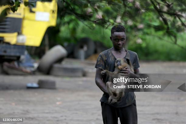 Boy plays with a monkey in the courtyard of a private residence in the Moanda district in Franceville on November 21, 2020. - Working in remote...