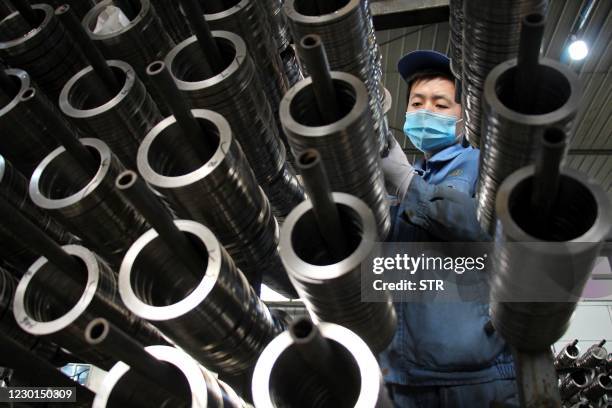 This photo taken on December 15, 2020 shows a worker placing aluminum pistons for vehicle engines on a production line at a machine manufacturing...