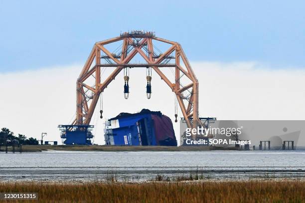 The Golden Ray cargo ship lies on its side in the water under a heavy-lift-twin-gantry catamaran near the St. Simons Island Pier. A salvage company...