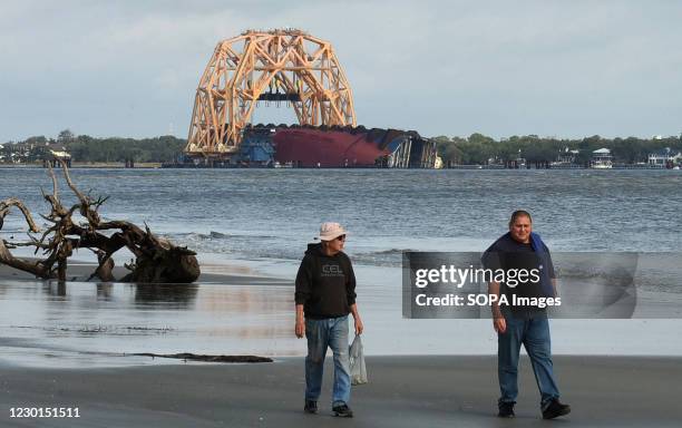 The Golden Ray cargo ship lies on its side in the water under a heavy-lift-twin-gantry catamaran near the St. Simons Island Pier. A salvage company...