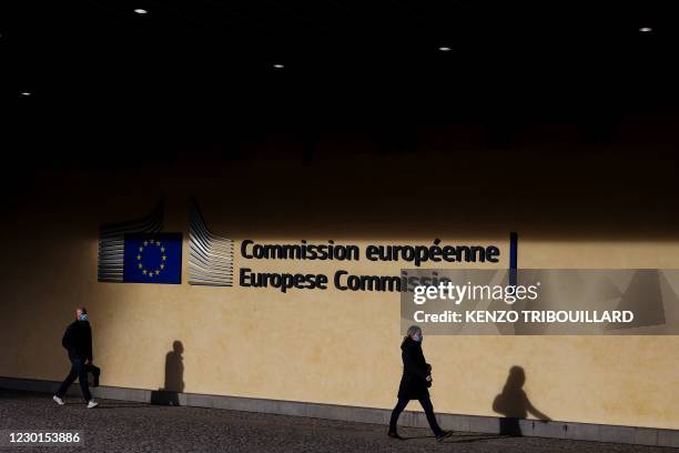 Persons wearing protective face masks walk outside the Berlaymont building, at the headquarters of the European Commission in Brussels on December...