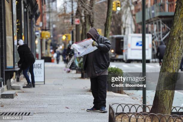 Worker scatters a bag of salt outside a business in New York, U.S., on Wednesday, Dec. 16, 2020. A major winter storm is zeroing in on more than 51...