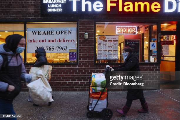 Pedestrians pass in front of a sign that reads "We are Open. Take out and delivery" outside a restaurant in New York, U.S., on Wednesday, Dec. 16,...