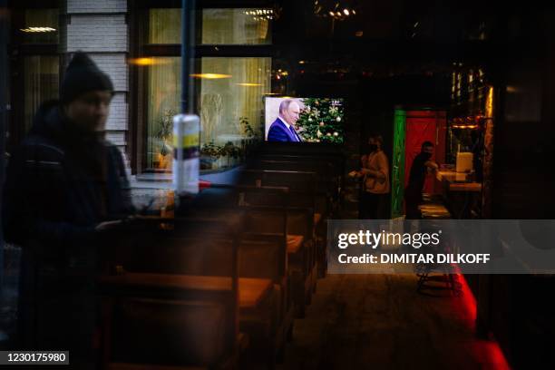 This picture taken through a restaurant window shows a TV screen showing Russian President Vladimir Putin addressing his annual press conference via...