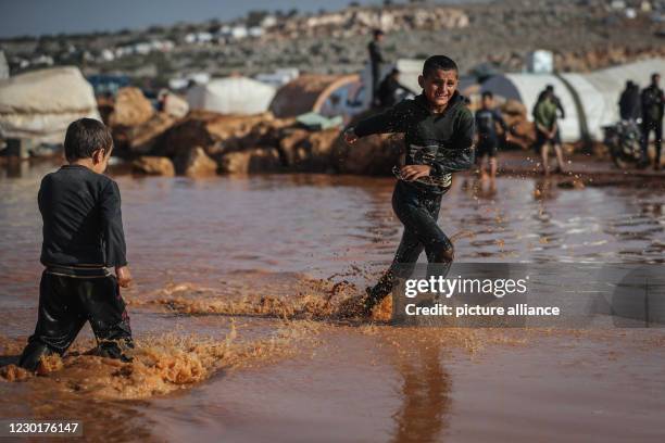 December 2020, Syria, Kafr Aruq: Two Syrian boys play amidst the muddy water after their tents have been flooded as a result of heavy rain at a...