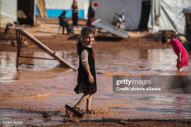 December 2020, Syria, Kafr Aruq: A Syrian girl wades through the muddy water in front of tents that have been flooded as a result of heavy rain at a...