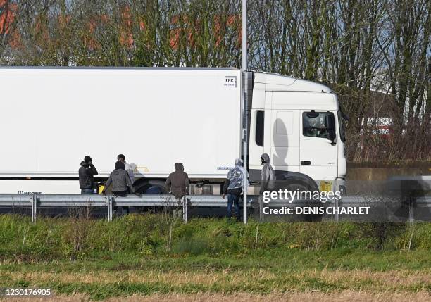 Migrants wait to climb into the back of lorries bound for Britain while traffic is stopped upon waiting to board shuttles at the entrance to the...