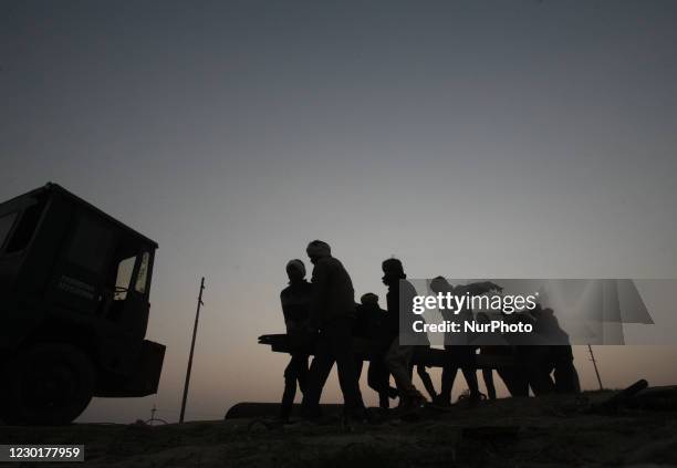 Workers carry an iron bar which is used in making temporary pantoon tank bridge over Ganges river , for the upcoming month long Annual magh mela...